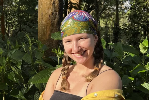Julie smiling outdoors, wearing a colorful headscarf — queer, non-binary full-spectrum and postpartum doula in NYC.