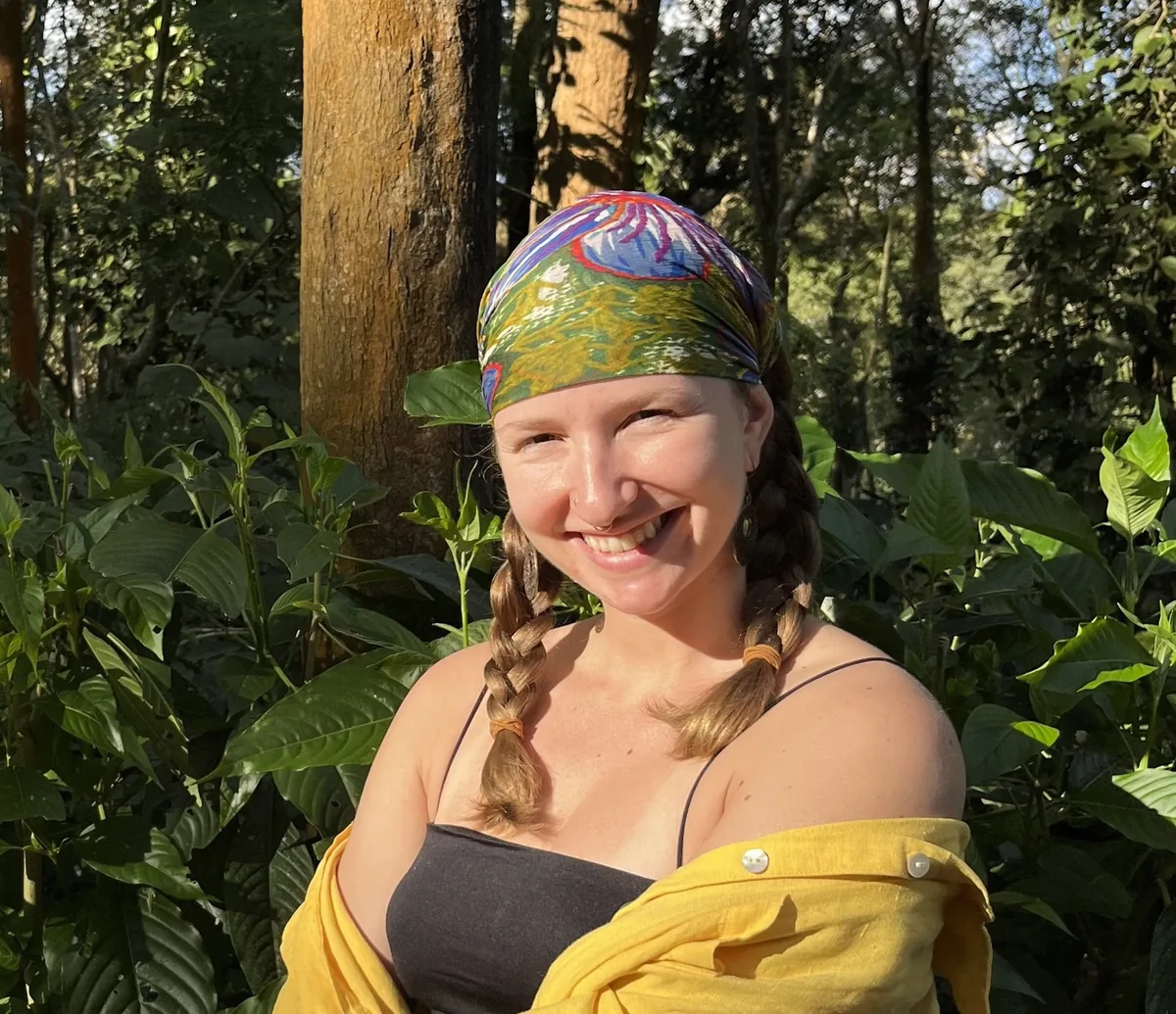 Julie smiling outdoors, wearing a colorful headscarf — queer, non-binary full-spectrum and postpartum doula in NYC.