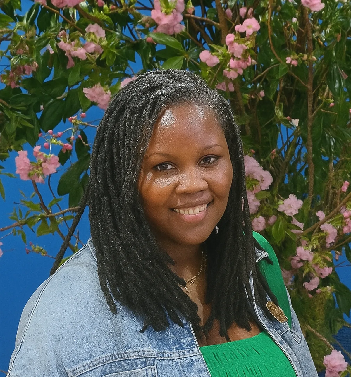 Tascha, postpartum doula in New York, smiling in front of pink flowering branches.