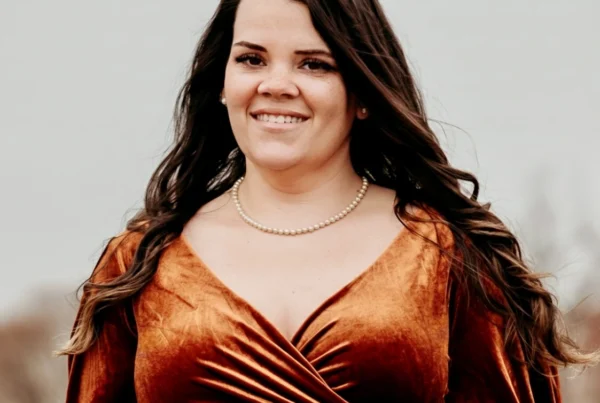 Portrait of Ireta, a birth and postpartum doula, smiling outdoors while wearing a rust-colored dress and pearl necklace.