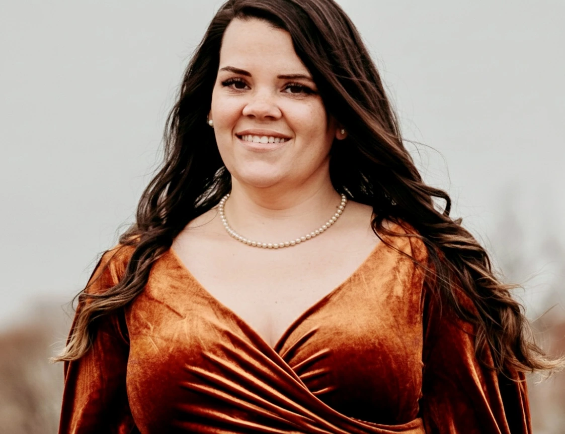 Portrait of Ireta, a birth and postpartum doula, smiling outdoors while wearing a rust-colored dress and pearl necklace.