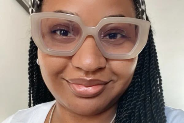 Johanny, a full-spectrum doula with braided hair and oversized translucent glasses, smiling warmly.