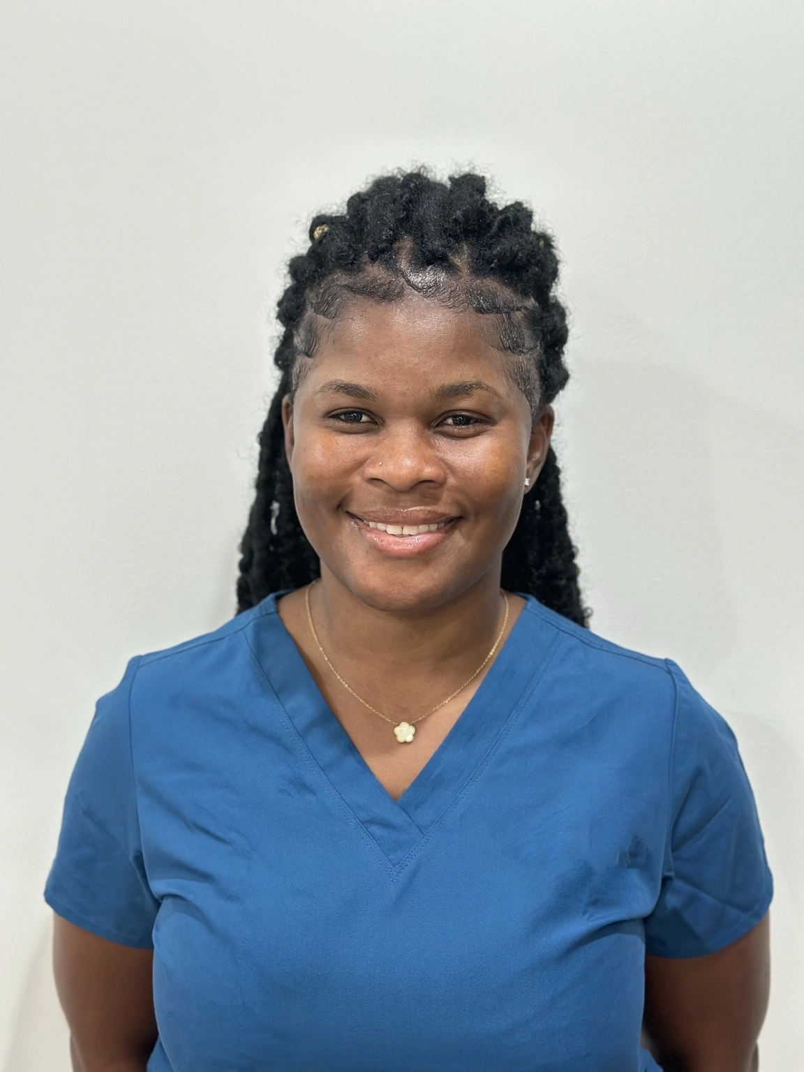 Sydia, postpartum doula with over 13 years of experience, smiling and wearing blue scrubs against a light background.