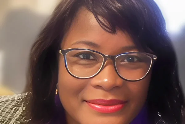 Professional portrait of Tracy, a certified postpartum doula in New York, smiling warmly while wearing glasses.